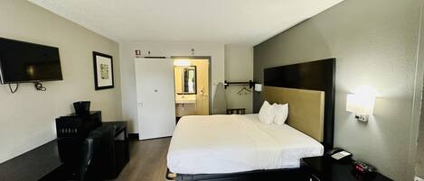Habitación de hotel con cama, escritorio, silla, televisión y baño visible a través de una puerta abierta.