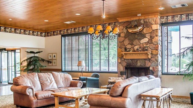 A spacious living room with leather sofas, a stone fireplace, and large windows with blinds. - Quality Inn Rhinelander (Rhinelander)
