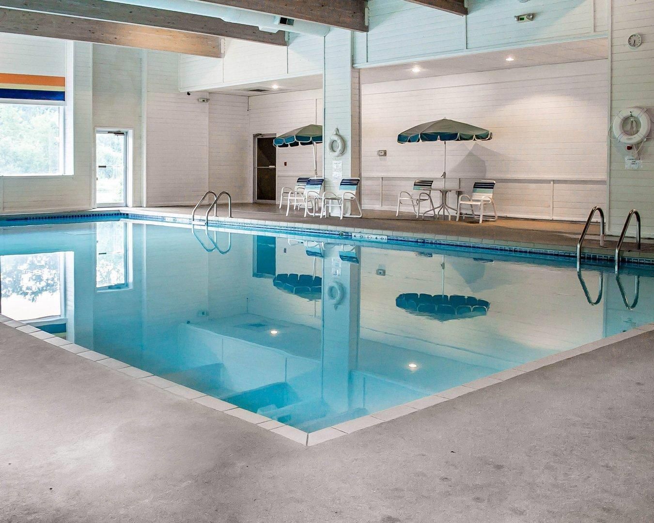 An indoor swimming pool with clear water, surrounded by lounge chairs and umbrellas.