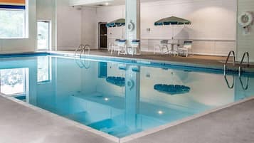 An indoor swimming pool with clear water, surrounded by lounge chairs and umbrellas.
