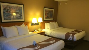 A hotel room with two beds, each with white bedding and brown decorative pillows. There are two wall-mounted lamps on the nightstands, and two framed pictures on the walls. - Quality Inn Rhinelander (Rhinelander)