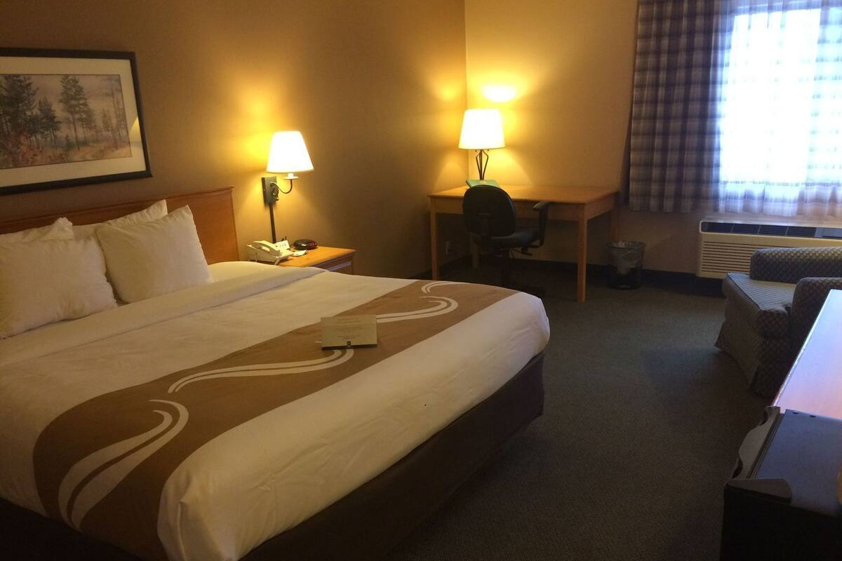 A hotel room with a large bed, two bedside lamps, a desk with a chair, and a window with curtains.
