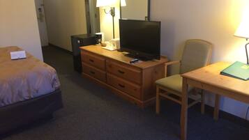 Une chambre d’hôtel comprenant un lit, une commode en bois, une télévision, un bureau avec une chaise et une lampe.