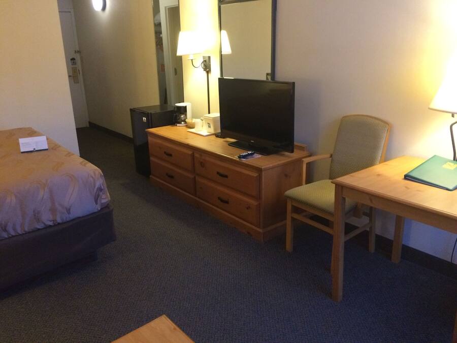 Une chambre d’hôtel comprenant un lit, une commode en bois, une télévision, un bureau avec une chaise et une lampe.