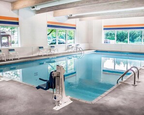 An indoor swimming pool with clear windows, a lifeguard stand, and seating along the poolside.