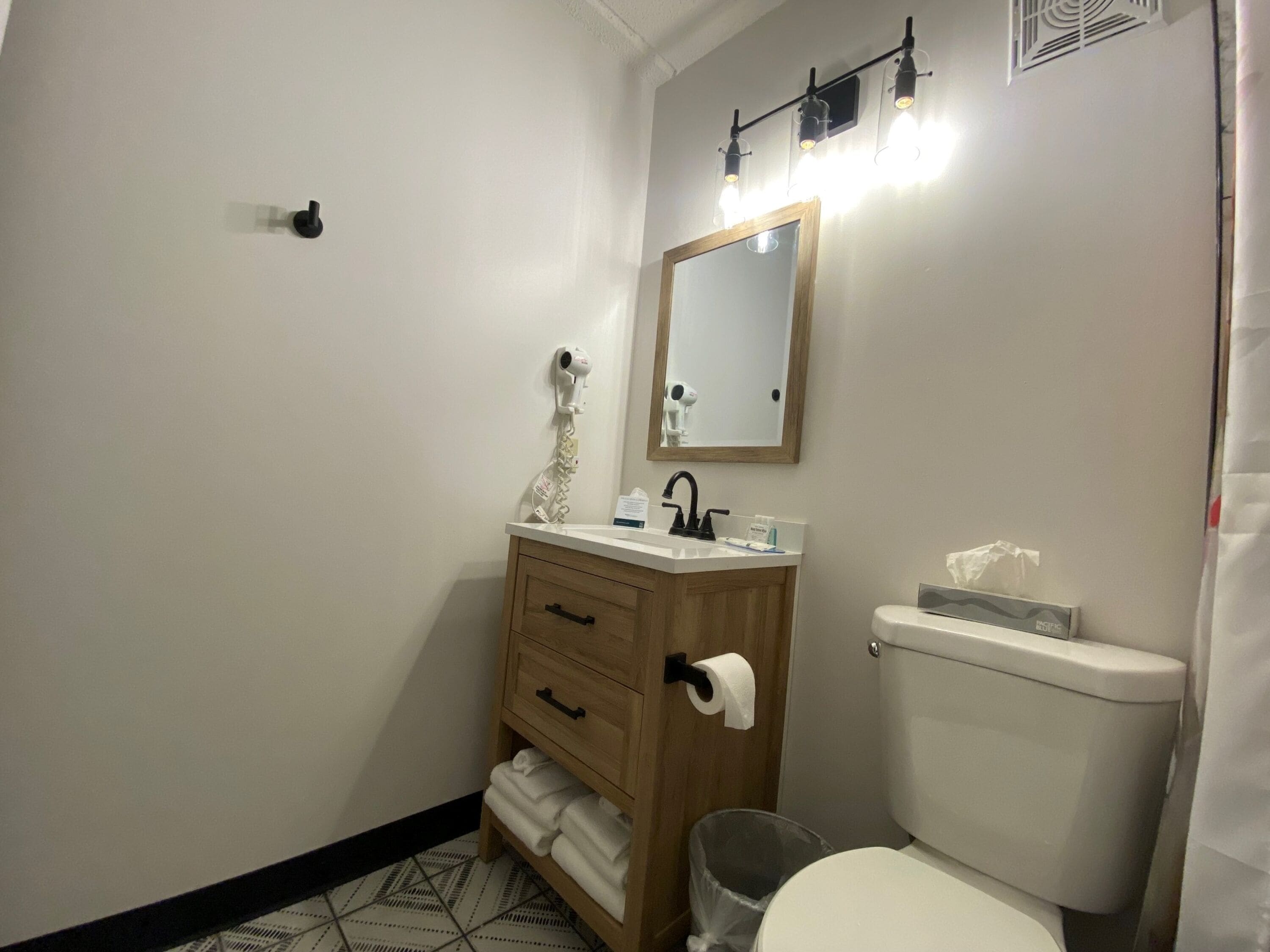 A bathroom with a wooden vanity, a mirror, a toilet, and a hairdryer.