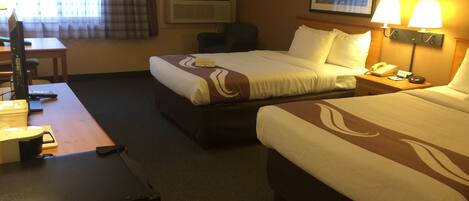 A hotel room with two beds, a desk, a chair, a lamp, and a painting on the wall.