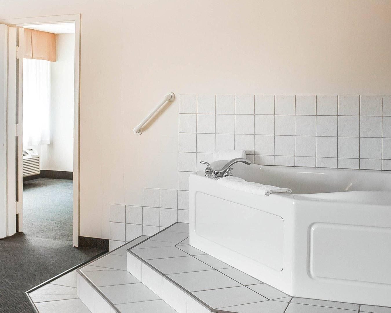 Une salle de bain moderne avec une baignoire, une barre d’appui et un sol carrelé.