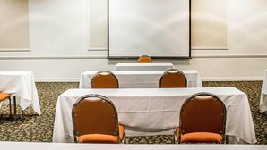 A conference room with white tables and orange chairs, a projector screen, and a carpeted floor. - Quality Inn Rhinelander (Rhinelander)