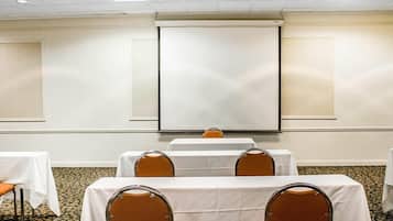 A conference room with white tables and orange chairs, a projector screen, and a carpeted floor.
