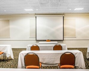 A conference room with white tables and orange chairs, a projector screen, and a carpeted floor.