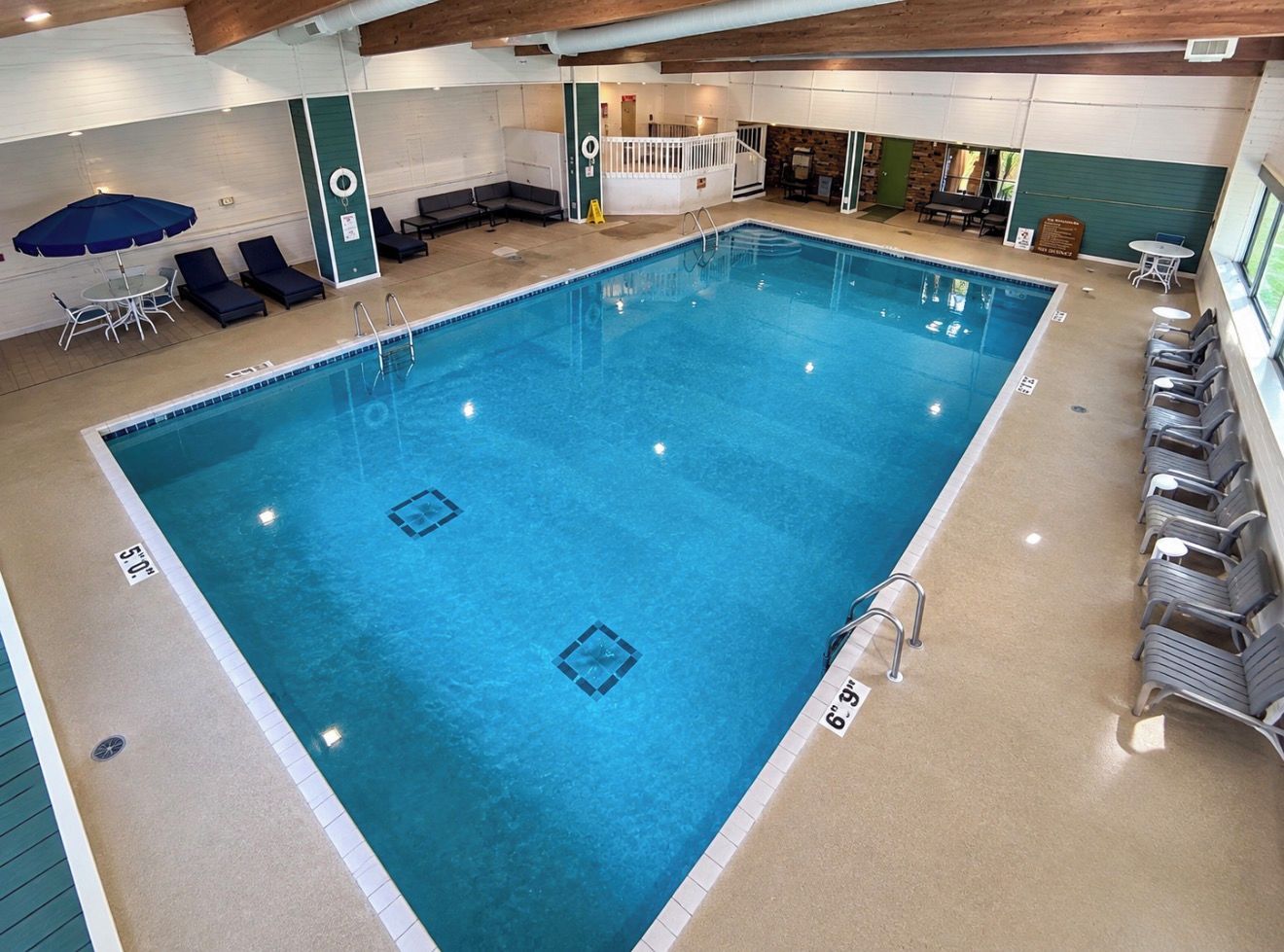 An indoor swimming pool with lounge chairs, a sunbed, and a lifeguard stand.