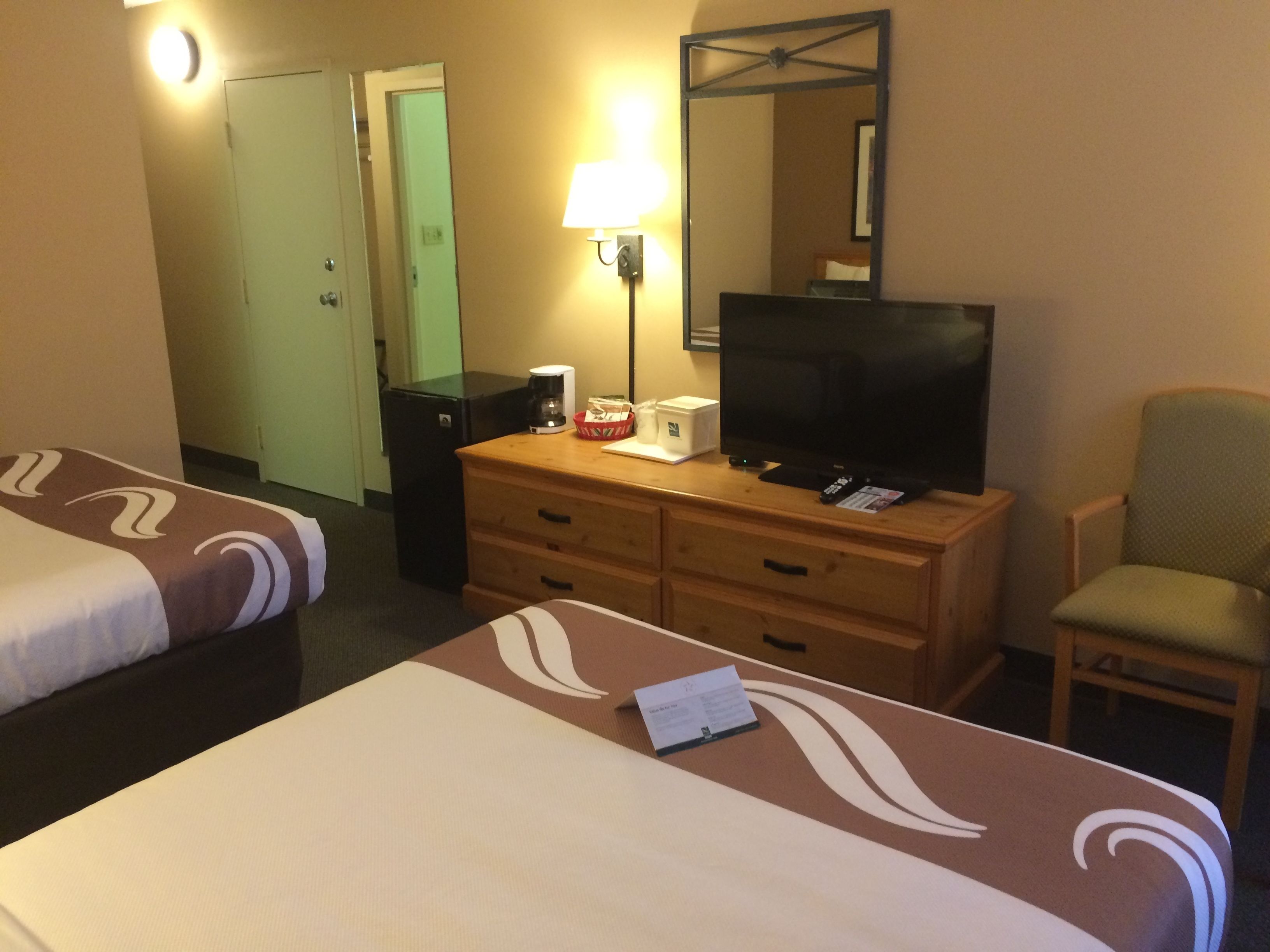 Habitación de hotel con dos camas, un televisor, un escritorio con cajones, una silla y una lámpara.