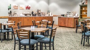 A hotel dining area with wooden tables and chairs, a counter with food and drink options, and a patterned carpet. - Quality Inn Rhinelander (Rhinelander)