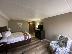 A hotel room with a bed, a desk with a lamp, a television, a chair, and a staircase leading to another room.