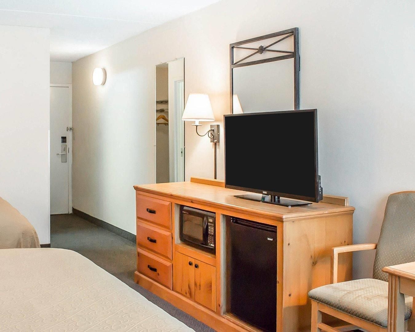 A hotel room with a bed, a wooden dresser with a television, a mirror, and a chair.
