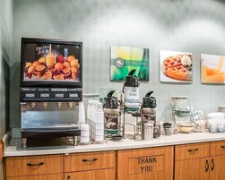 Un dispensador de zumos con varias opciones, una máquina de café y un cartel que dice 'Gracias' sobre una encimera.