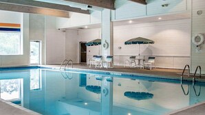 An indoor swimming pool with clear water, surrounded by lounge chairs and umbrellas, and a view of the outside through a large window. - Quality Inn Rhinelander (Rhinelander)
