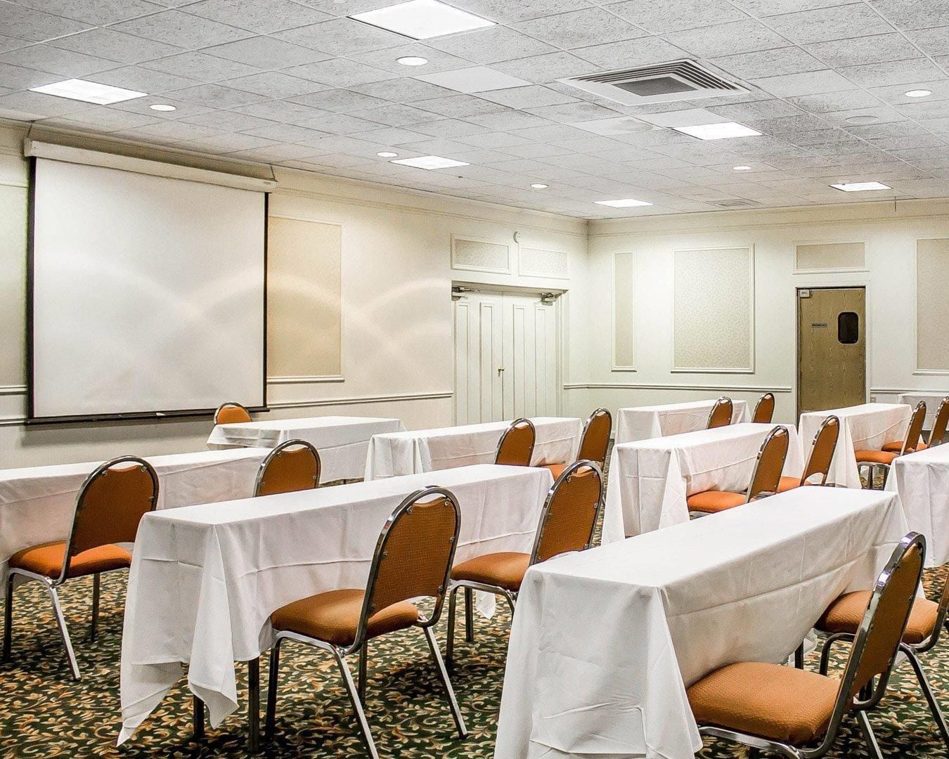 A conference room with rows of tables and chairs, a projection screen, and a door.