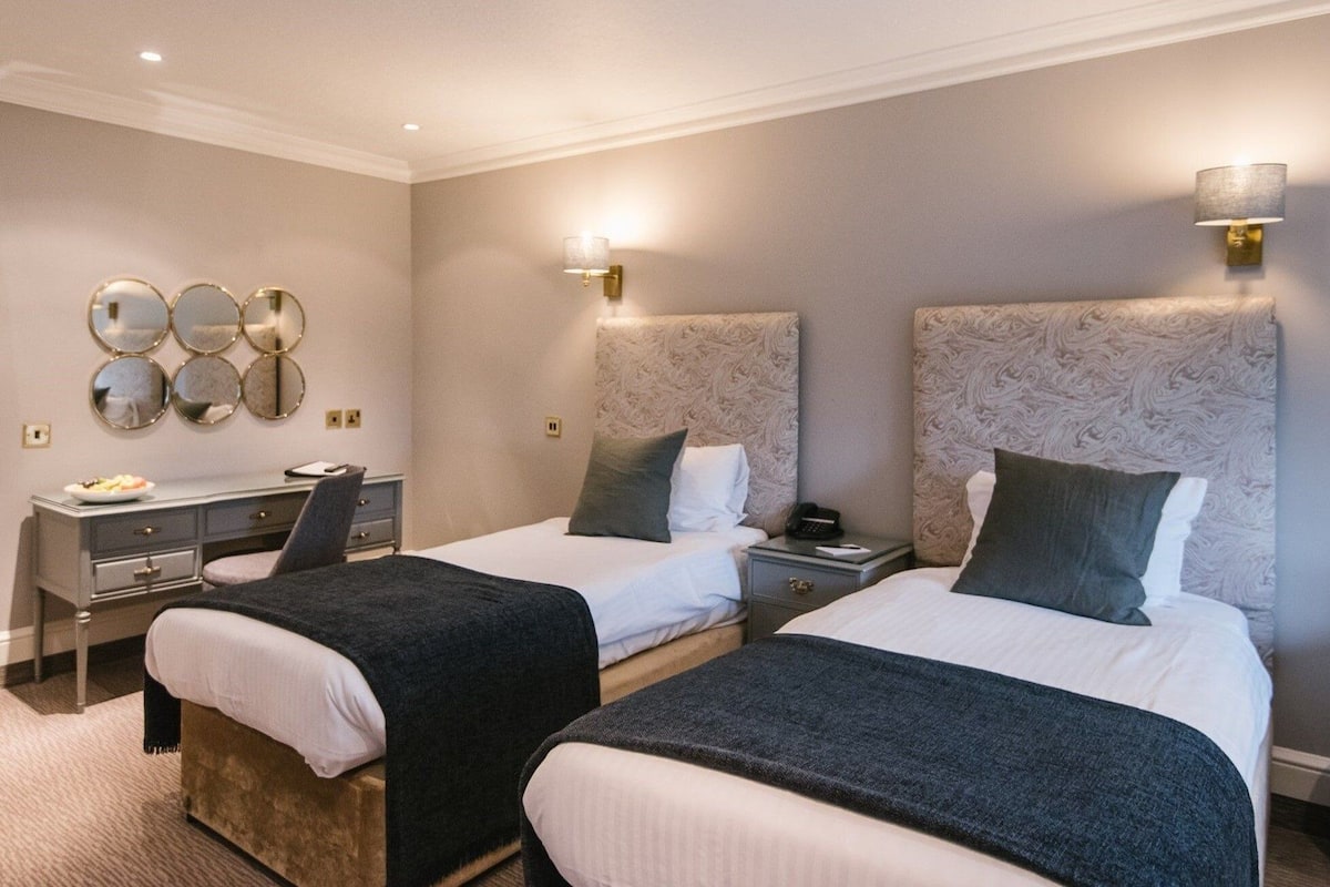 Habitación de hotel con dos camas, un escritorio y una pared espejo.