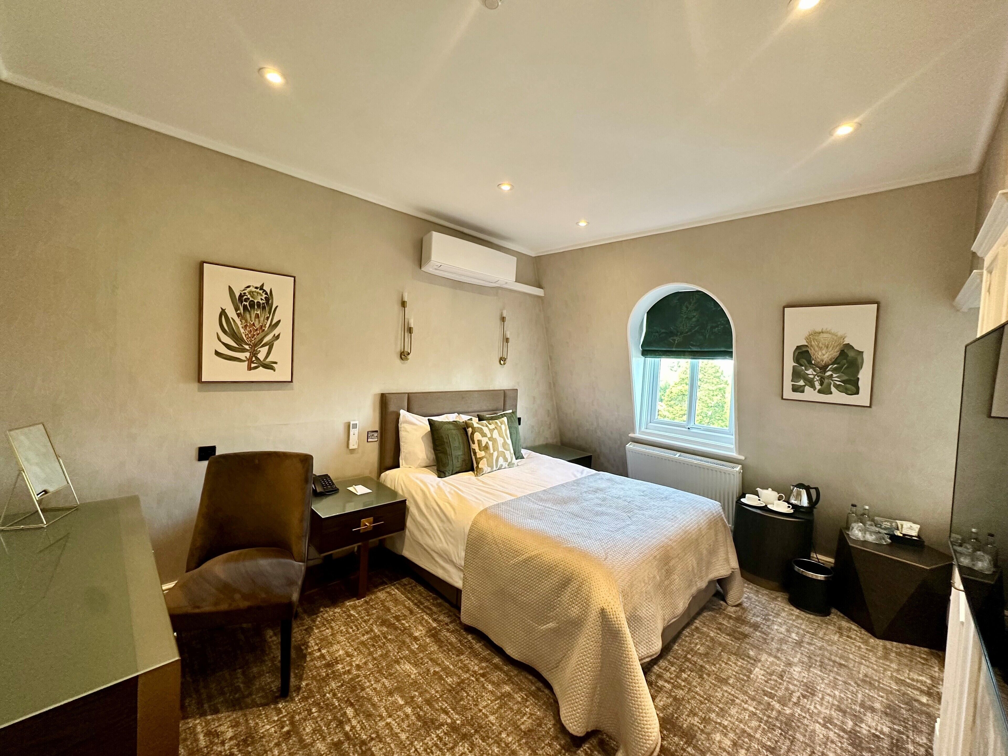 A hotel room with a bed, a desk, a chair, a window with a view, and artwork on the walls.