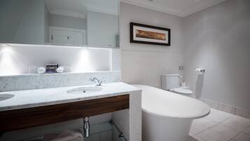 A modern bathroom with a marble sink, wooden vanity, a large mirror, a framed picture on the wall, and a standalone bathtub.