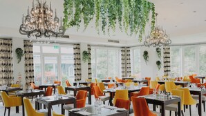 A spacious dining area with multiple tables and chairs, large windows, and hanging plants. - The Spa Hotel (Royal Tunbridge Wells)