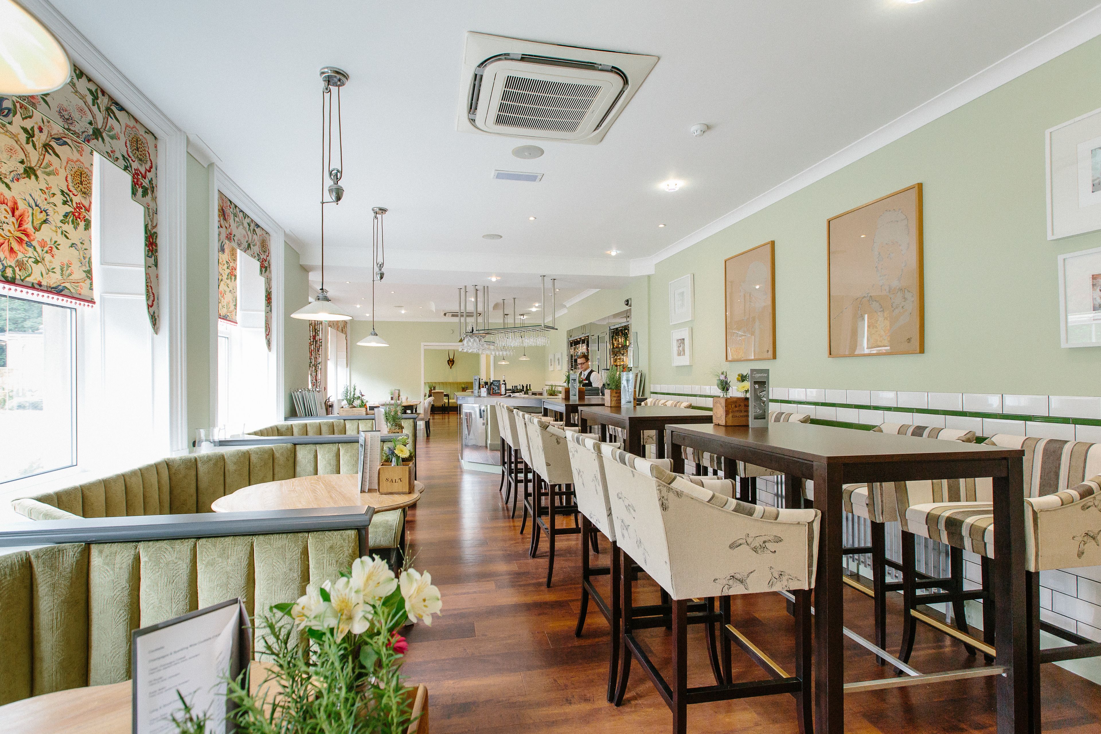 A restaurant with booths and high-top tables, wooden flooring, and pendant lighting.