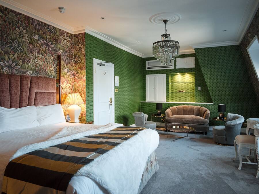 Een slaapkamer met een groot bed, een kroonluchter, een groene accentmuur en uitzicht op de lucht.