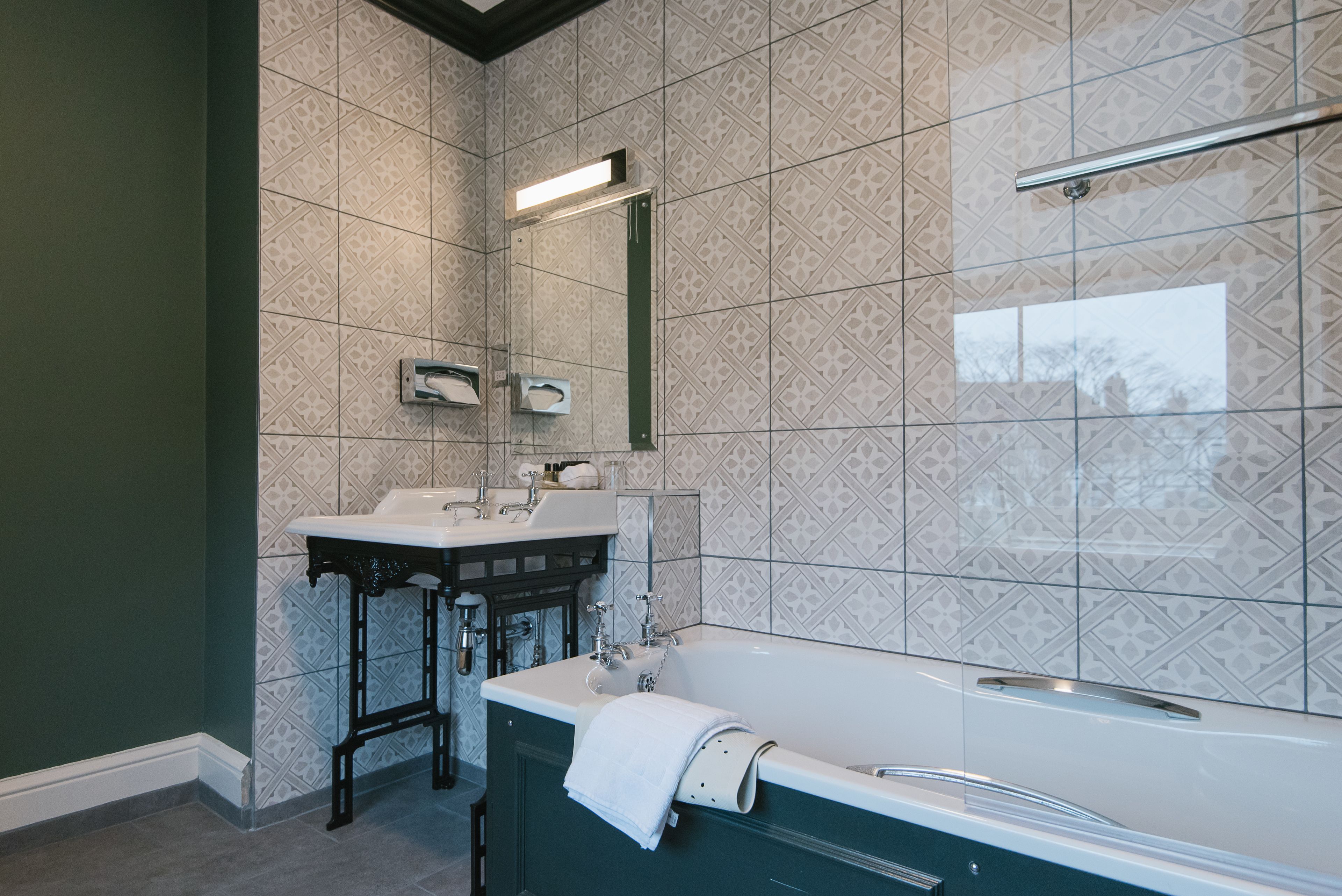 A bathroom with a freestanding bathtub, a vanity with a mirror, and patterned tile walls.