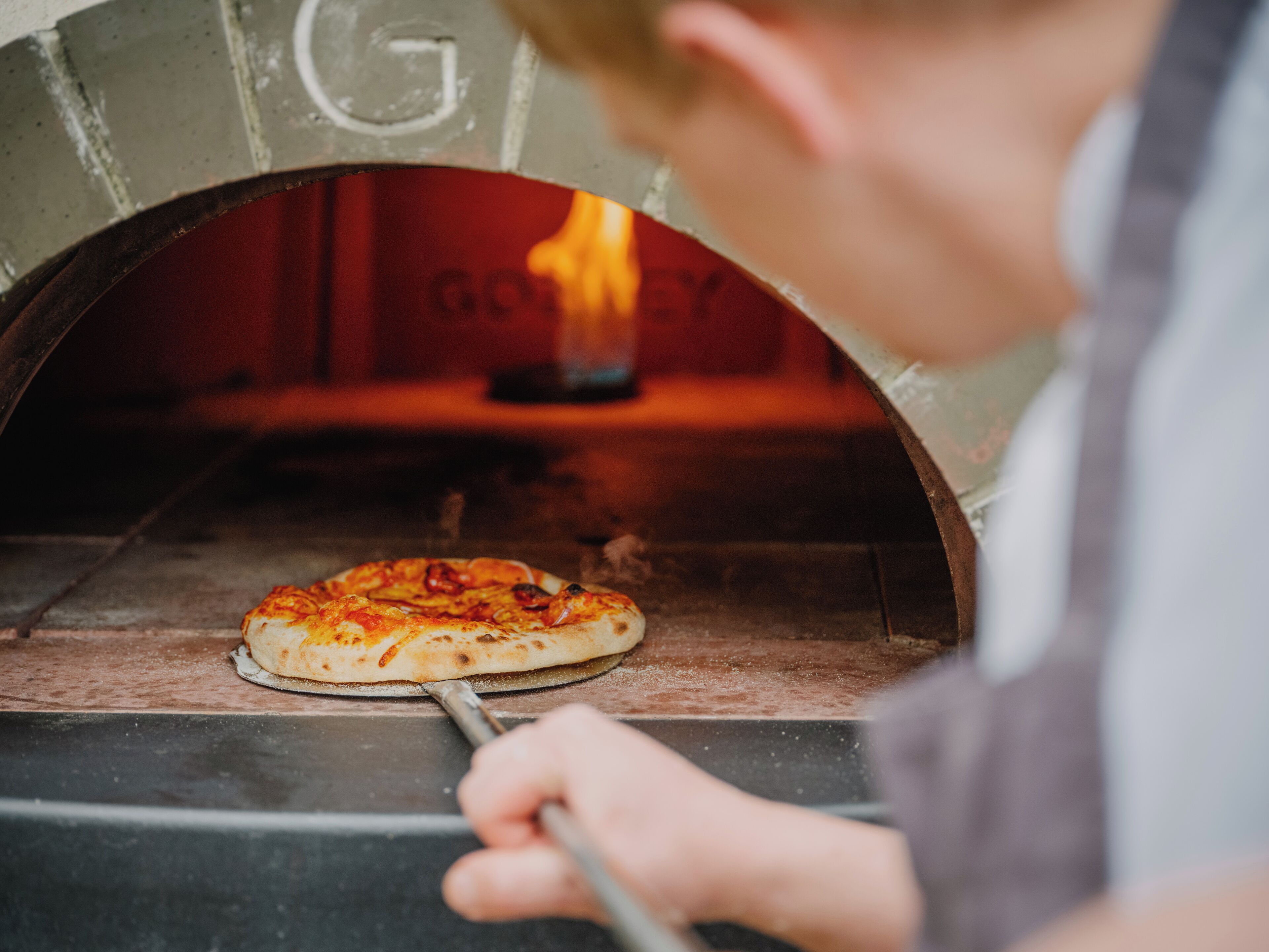 Una persona utilizando una pala para pizza para sacarla de un horno de ladrillo.