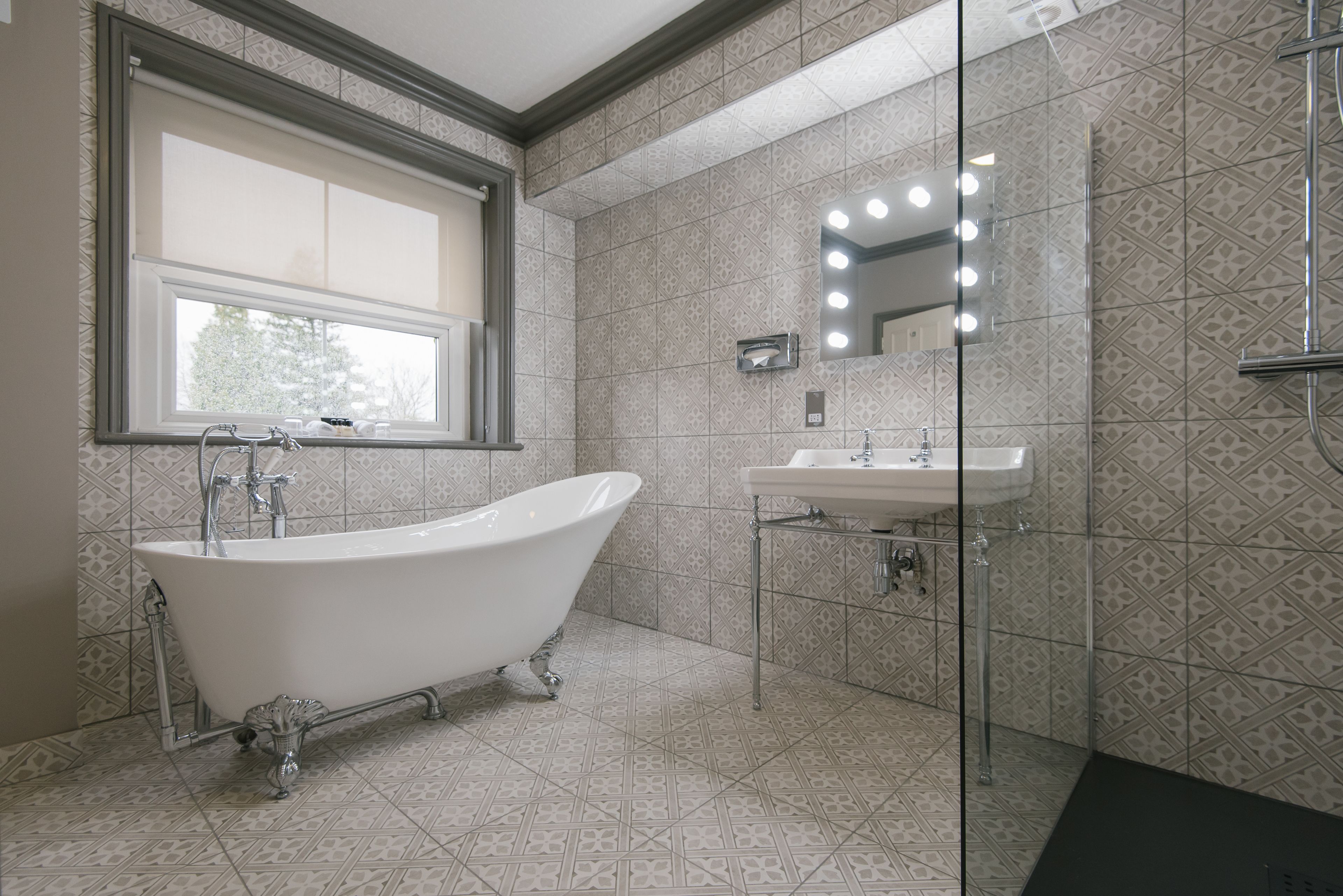 A bathroom with a freestanding bathtub, a sink, and a mirror with lights.