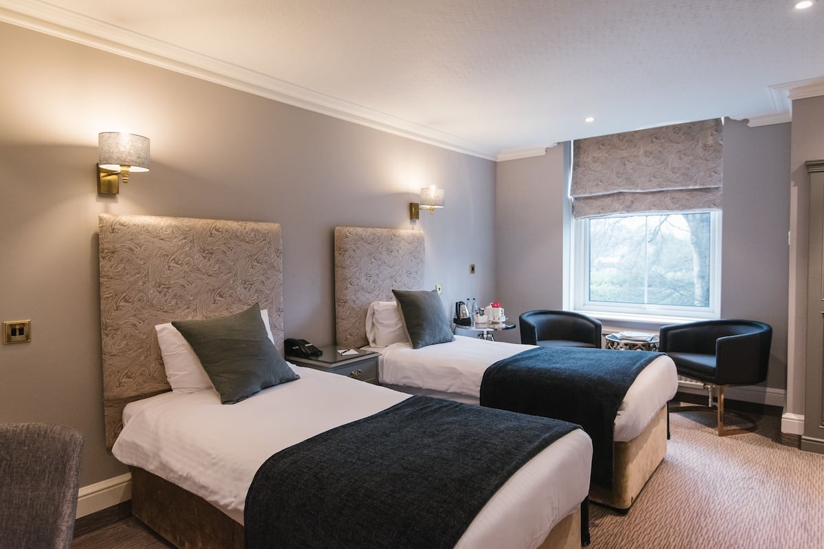 Habitación de hotel con dos camas, un escritorio, una silla y una ventana con vistas.