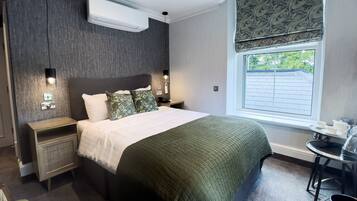 Ein modernes Hotelzimmer mit einem großen Bett, Nachttischen, einem kleinen Tisch mit Tassen sowie einem Fenster mit Blick und einer Klimaanlage.