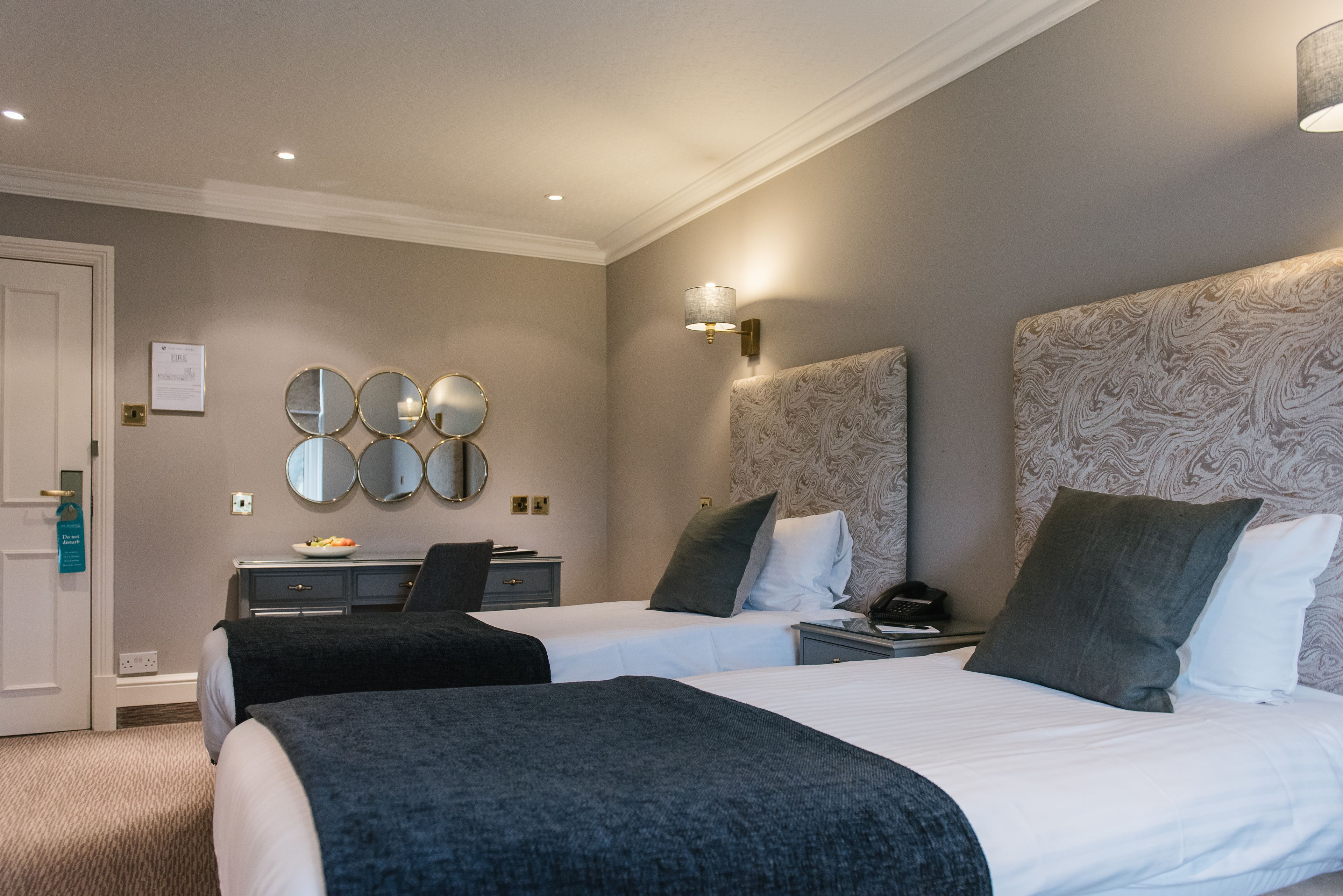 A hotel room with two beds, a desk, a chair, and a wall-mounted mirror.