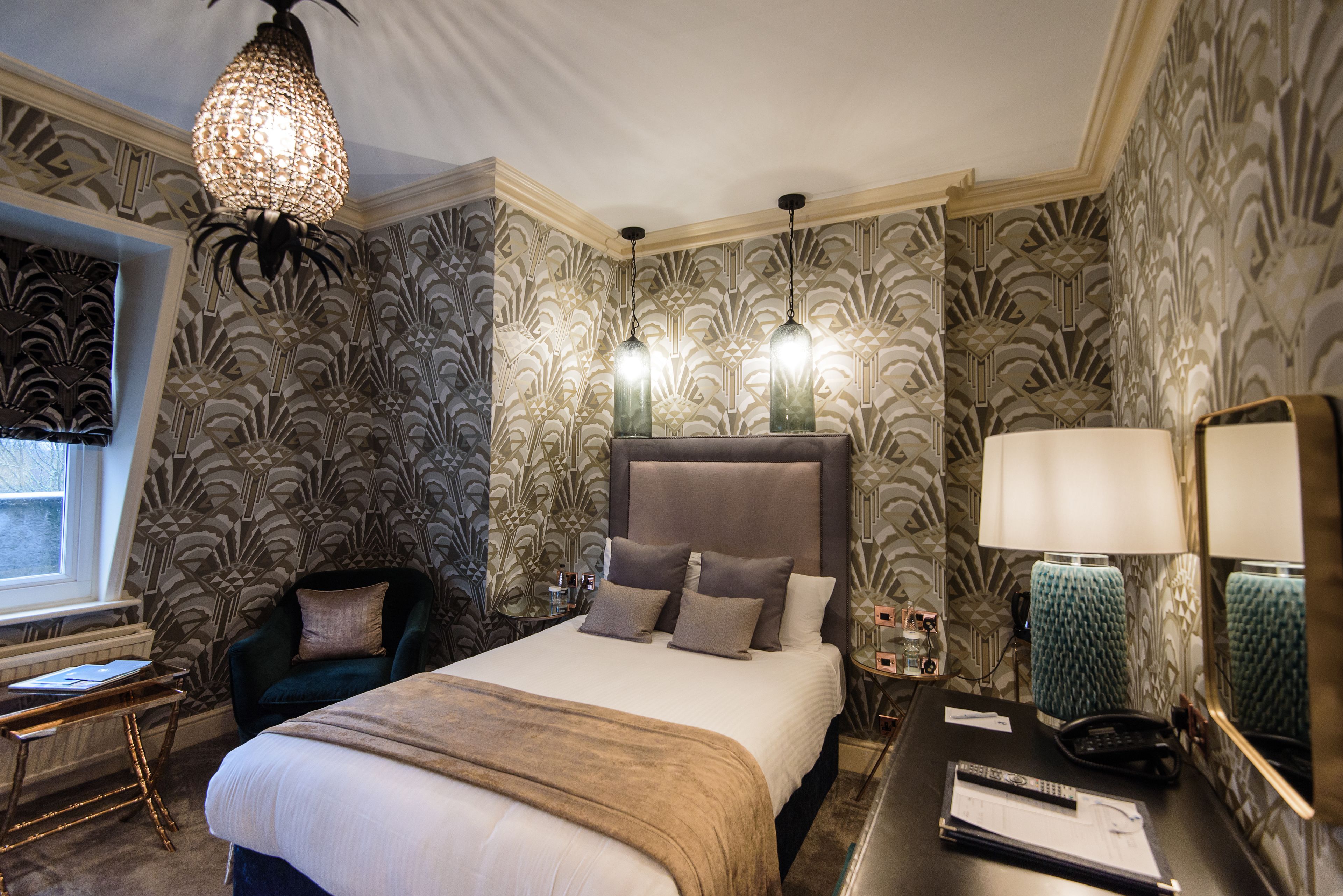 A hotel room with a large bed, a chair, a desk with a lamp, and a large mirror.