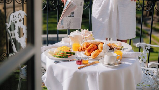 A breakfast table with a newspaper, fruits, pastries, and beverages, set on a balcony with a railing. - The Spa Hotel (Royal Tunbridge Wells)