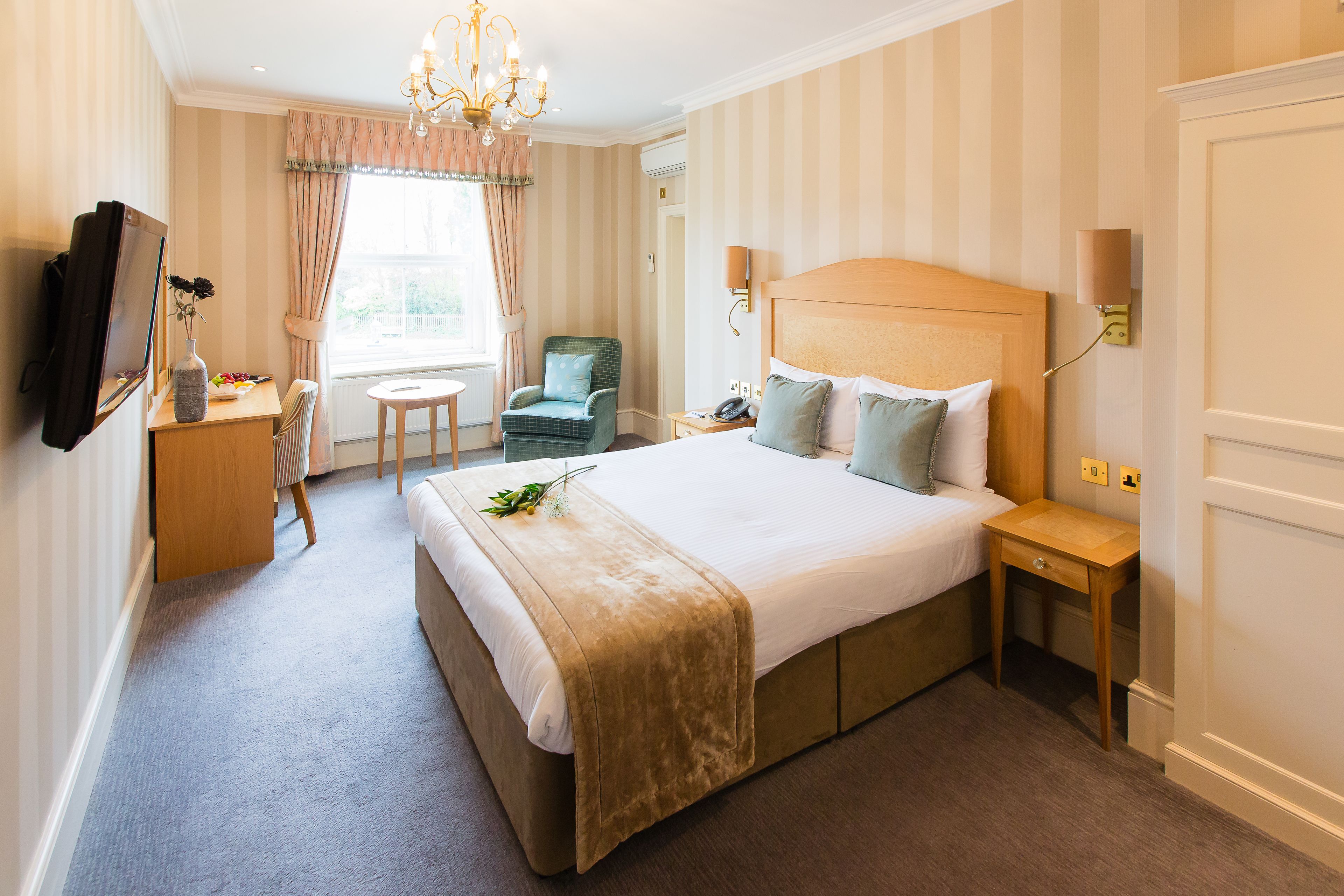 A hotel room with a large bed, a desk, a chair, a television, and a window with curtains.