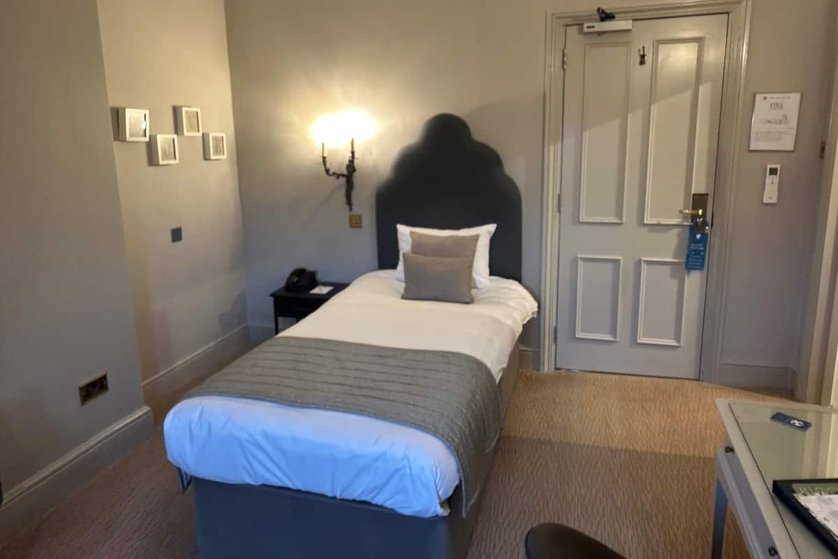 Una habitación de hotel con cama, mesita de noche, lámpara y una puerta con cerradura y lector de tarjetas.