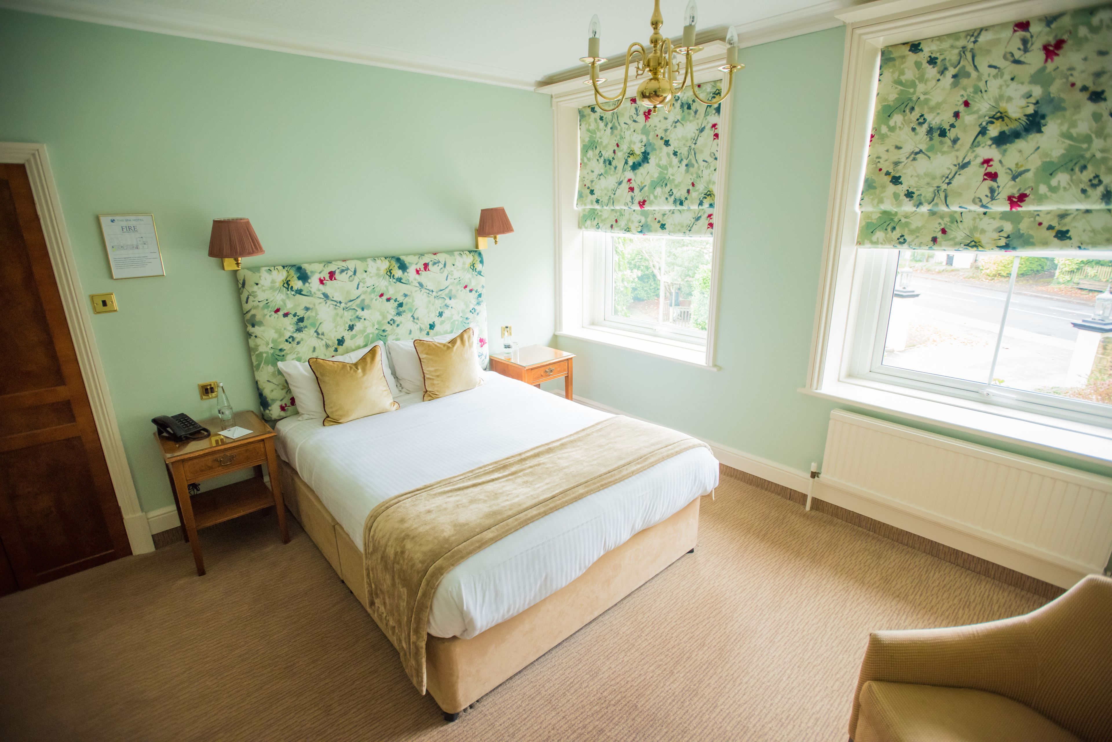 Un dormitorio con cama, mesitas de noche, una ventana con cortinas florales y un candelabro.