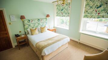 Un dormitorio con cama, mesitas de noche, una ventana con cortinas florales y un candelabro.
