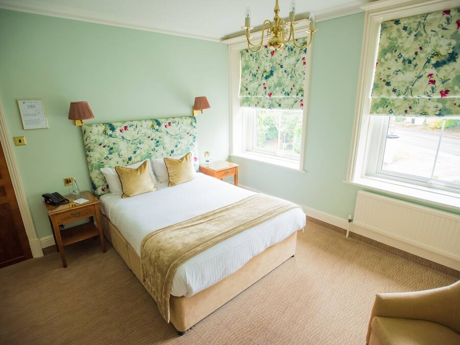 Ein Schlafzimmer mit einem Bett, Nachttischen, einem Fenster mit floralem Vorhang und einer Chandelier.