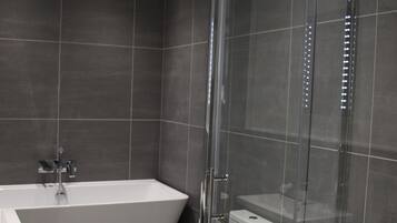 A modern bathroom with a glass-enclosed shower, a freestanding bathtub, and a toilet.