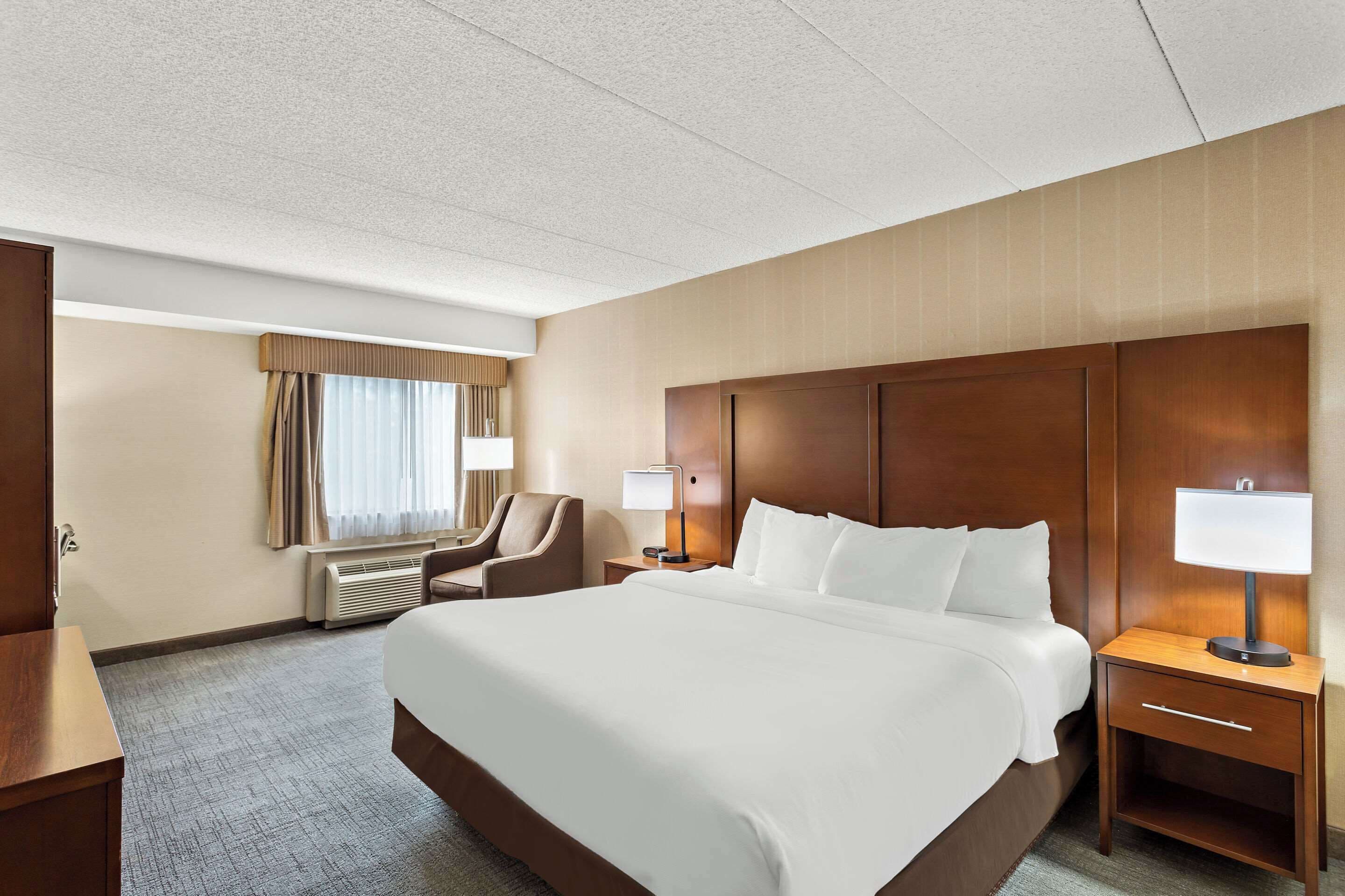Una habitación de hotel con una cama grande, dos mesitas de noche con lámparas, una silla, un escritorio y una ventana con cortinas.