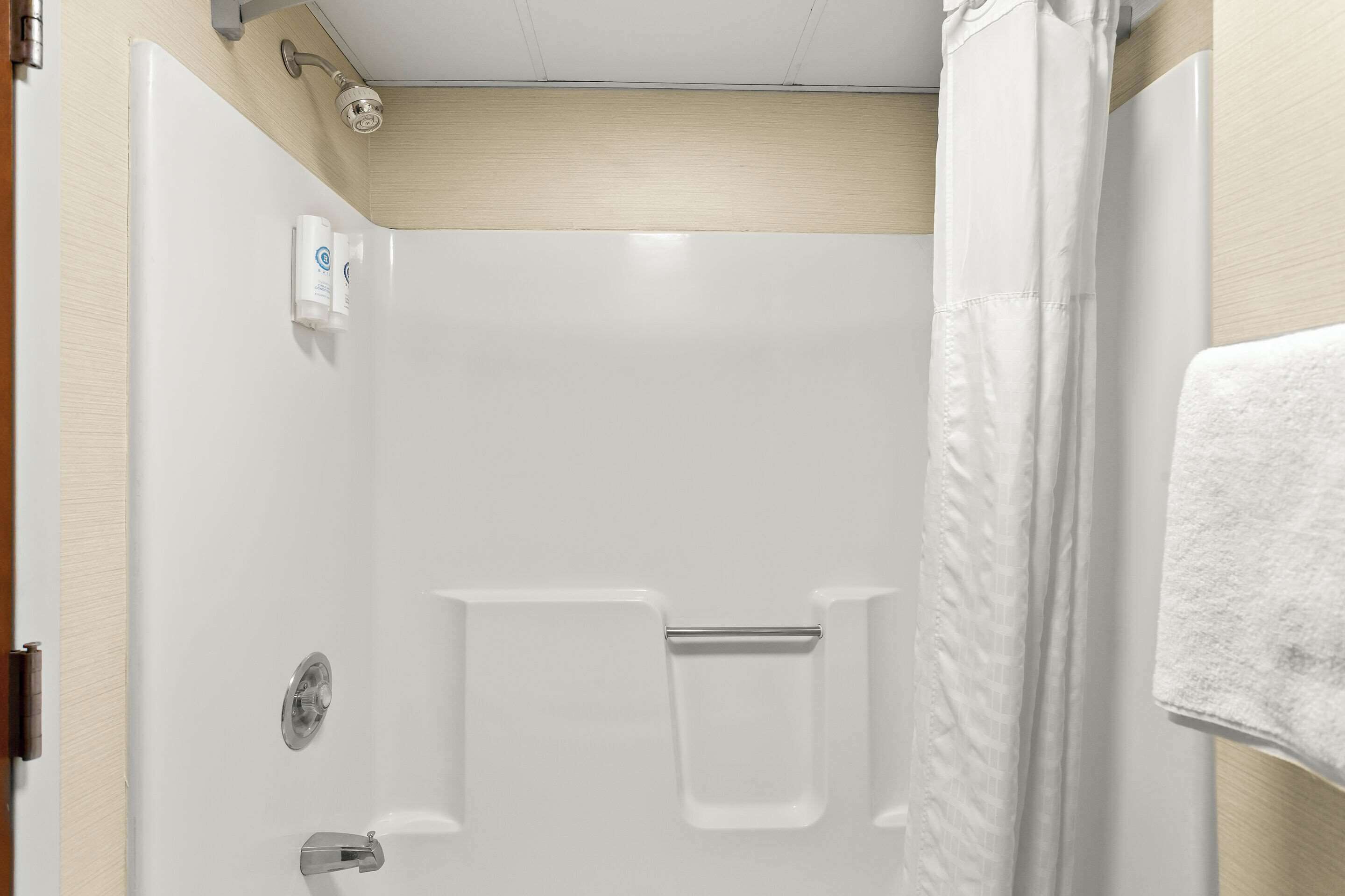 Un box de ducha blanco con cabezal, toallero y una toalla colgada en la pared.