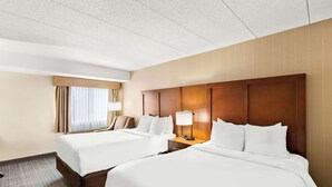 Habitación de hotel con dos camas, un cabecero de madera, una mesita de noche con lámpara y una ventana con cortinas.