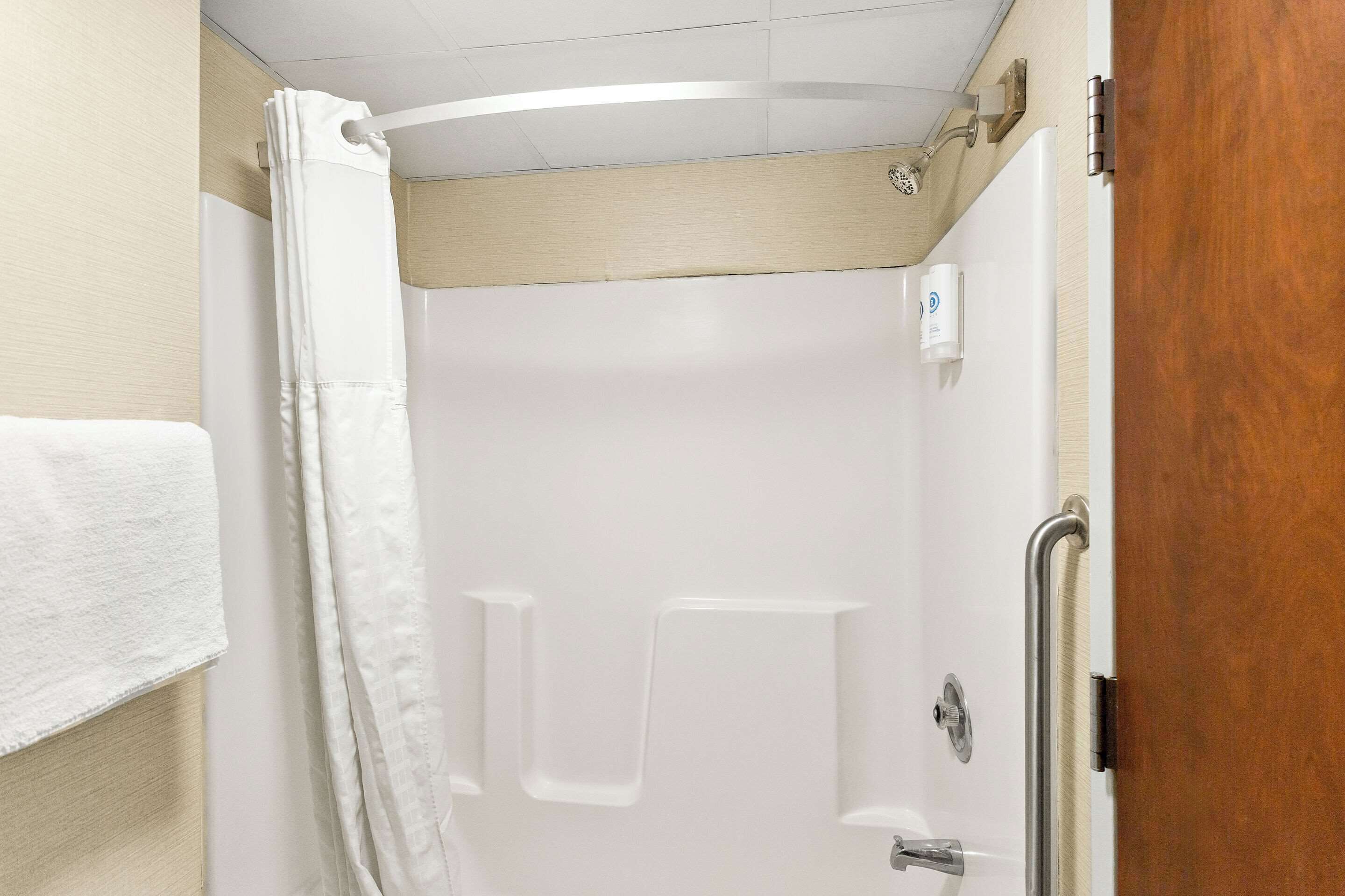 A shower stall with a white curtain, a handheld showerhead, and a grab bar.
