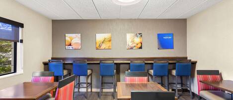 A restaurant with booths and high tables, featuring artwork on the wall and a ceiling light fixture.