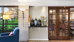 Zona de bar con dispensadores de café, una lámpara y un área de estar con una silla azul.