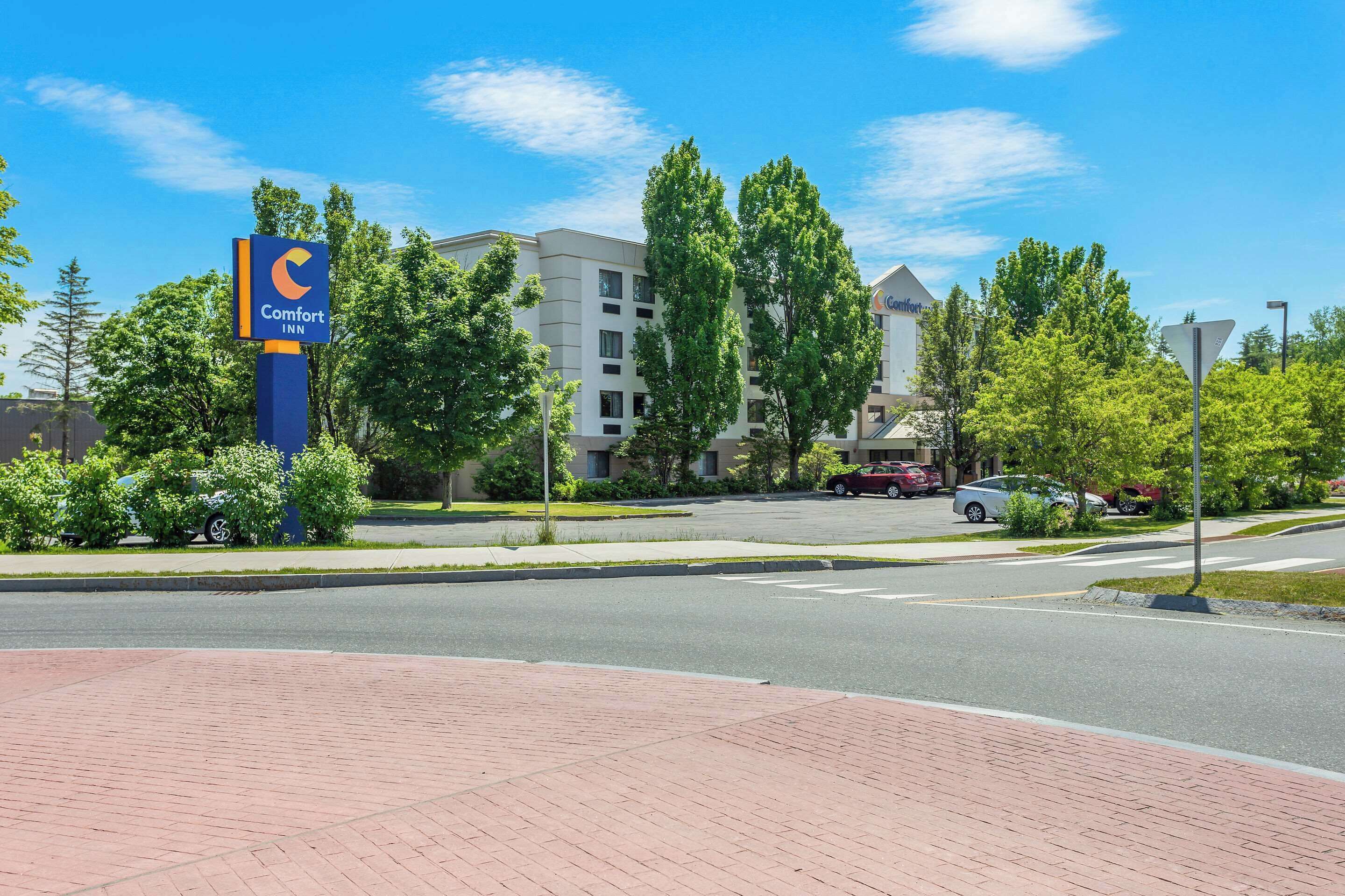 Um hotel Comfort Inn com um céu azul límpido, um caminho pavimentado e um estacionamento com vários carros.
